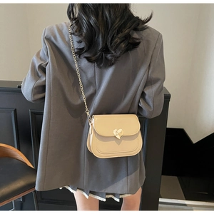 Detail of beige flap bag with gold heart clasp and chain strap on grey blazer