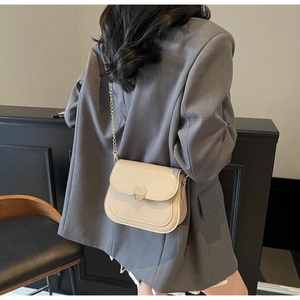 Detail of a cream saddle bag with heart-shaped gold buckle worn over a grey blazer