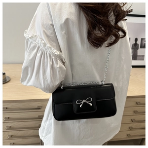 Detail of black leather crossbody bag with silver bow accent and metal chain strap