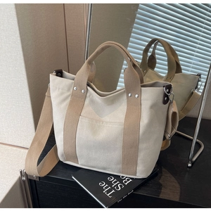 Dettaglio della borsa tote in tela con manici a contrasto e tracolla su uno specchio