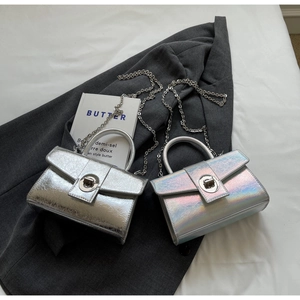 Detail of silver patent leather crossbody bags with metal chains on a grey blazer