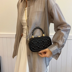 Bolso caja ovalado negro con bordado de corazón y cadena dorada mostrado en modelo