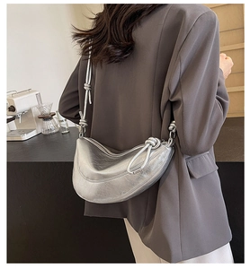 Detail of silver crescent bag with metallic pleats and knotted strap on gray blazer