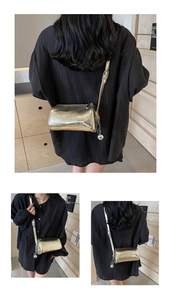 Detail of metallic gold cylinder bag with pleated texture and round metal ball charm
