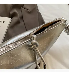 Detail of silver pleated shoulder bag with smooth zipper and knot charm design