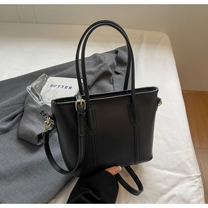 Détail du cabas en cuir noir avec ferrures dorées sur un tissu blanc minimaliste
