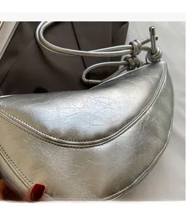 Close-up of metallic silver crescent bag with retro pleated leather and knotted shoulder strap