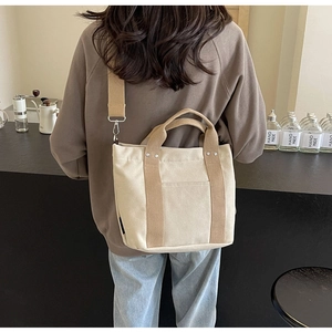 Borsa tote in tela beige con manici a contrasto e tracolla indossata da una modella al caffè