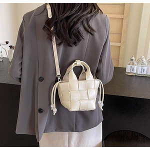 Détail d'un mini sac seau tressé beige porté par un mannequin dans un cadre de café