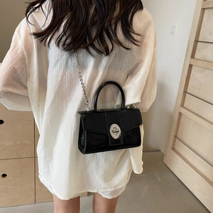 Black glossy patent leather crossbody bag with silver chain strap shown on a model