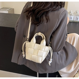 Détail du sac seau tressé crème avec cordon perlé porté sur un tailleur gris