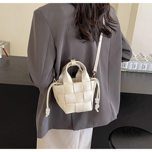 Modèle portant un sac seau tissé beige en cuir avec cordon de serrage et bandoulière