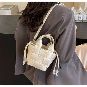 Détail du sac seau tressé crème avec fermeture à cordon et perles en acrylique
