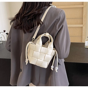 Vue détaillée d'un sac seau tressé crème avec bandoulière réglable porté par un mannequin