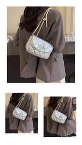Detail view of silver quilted crossbody bag with gold chain strap on grey blazer