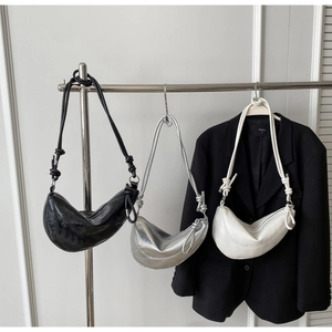 Detailed view of three crescent hobo bags in black, silver, and white with knot handle detail
