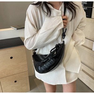 Detail view of black moon shoulder bag featuring crinkled patent leather and knot strap