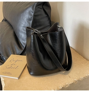Détail du sac seau noir montrant le cuir à texture craquelée et le logo minimaliste