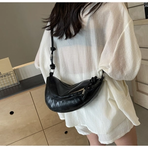 Detail of minimalist black crescent crossbody bag with glossy finish and knotted strap