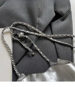 Detailed macro view of glossy silver pleated bucket bag with adjustable metal chain strap