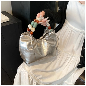 Detail of silver metallic bucket bag with textured surface and colorful bead handle