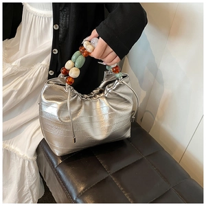 Detail of silver metallic handbag featuring textured fabric and colorful acrylic beaded handle