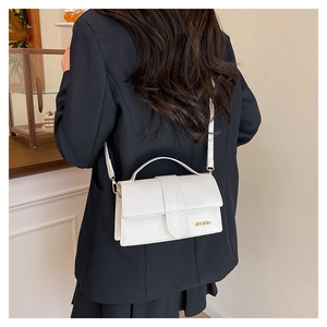 Detailed view of the white crossbody bag featuring a golden metal logo on a leather flap