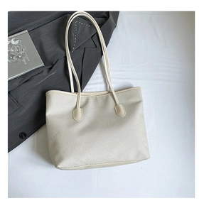 Flat lay of woven tote bag with leather trim alongside a grey blazer and magazine