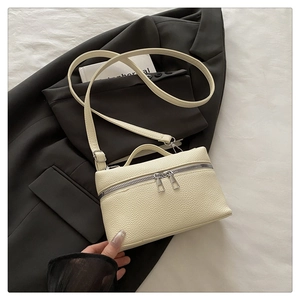 Détail du sac à main crème en cuir grainé avec double fermeture éclair argentée sur veste
