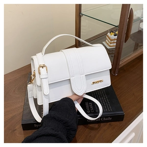 Detail of white square handbag showing golden metal logo and premium leather texture