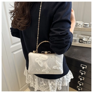 Detail of white evening bag featuring lace floral patterns and rhinestone butterfly clasp