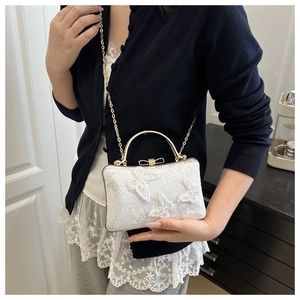 Detail of white lace evening bag featuring 3D butterfly embroidery and metal handle