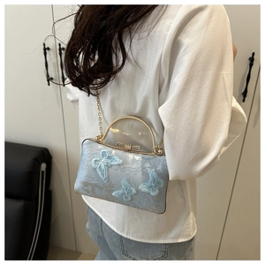 Detail of light blue evening bag with butterfly embroidery and golden metal handle