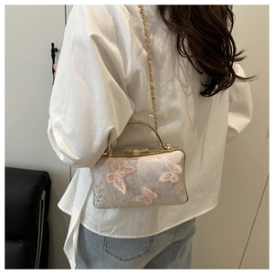 Detail of floral lace embroidery and pink butterfly 3D motifs on a white evening bag