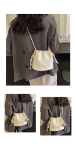 Detail of white glossy bucket bag showing metal triangle logo and chain strap