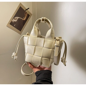 Détail d'un sac à main tressé beige avec cordon de serrage et finitions dorées