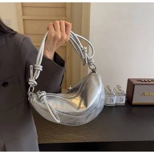 Close-up of silver crescent bag with textured pleats and knotted woven handle detail