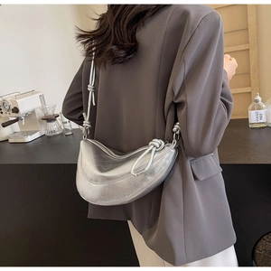 Close-up of a silver crescent bag featuring matte metallic texture and stylish knot detail