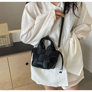 Détail d'un sac seau tressé noir montrant la texture du cuir et la bandoulière amovible
