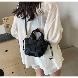 Détail d'un sac seau tressé noir avec de larges bandes en cuir et cordon de perles blanches