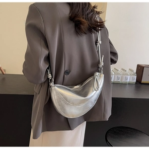 Detail of silver metallic crescent bag featuring knot strap and textured finish on a model