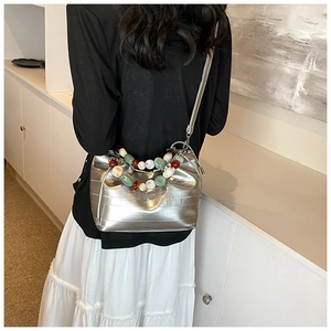 Detail of silver crossbody bucket bag with colorful decorative beaded handle shown on model