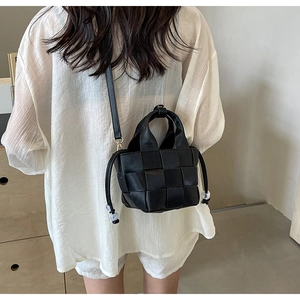Détail d'un sac seau tressé noir avec bandoulière et cordon de serrage orné de perles