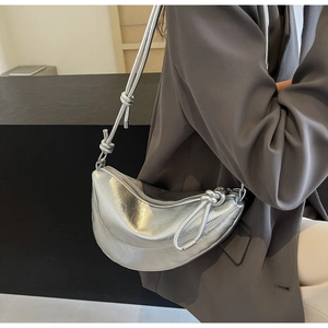 Detail of silver metallic crescent bag featuring unique knot design on the shoulder strap