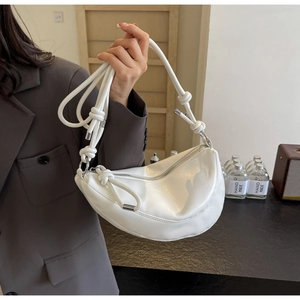 Detail of white half-moon shoulder bag with knotted strap and metallic hardware