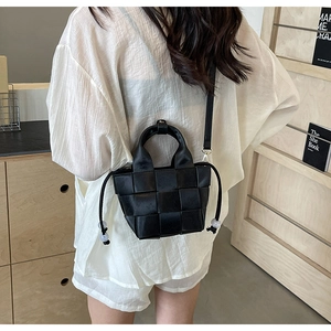 Détail d'un sac seau tissé noir avec un motif à grand treillis et cordon à pompons