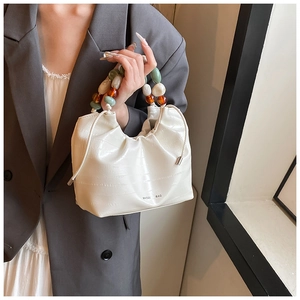 Detail of off-white bucket bag featuring crocodile texture and colorful beaded handle