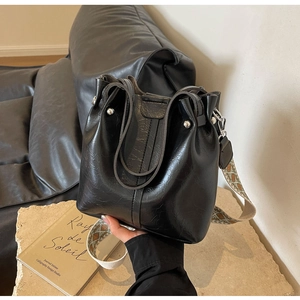 Detail der schwarzen Beuteltasche aus Leder mit Nieten und ethnischem Web-Schultergurt
