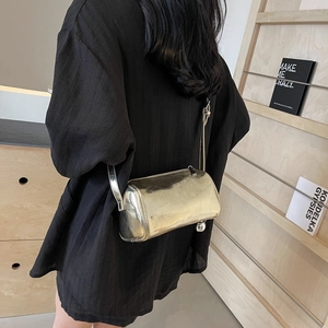Silver metallic pillow bag with cylindrical shape and adjustable crossbody strap on model