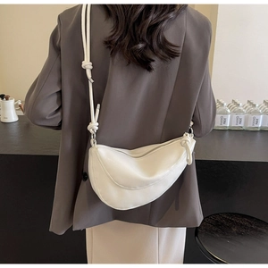 Close-up of white croissant-style crossbody bag with knotted strap and silver zipper